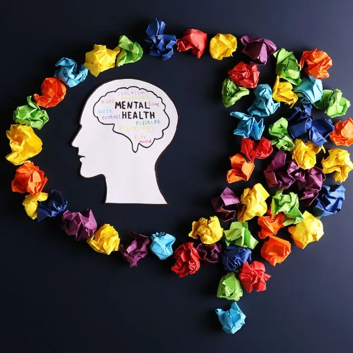 La imagen representa el concepto de la salud mental de forma creativa y colorida. Se observa el contorno de una cabeza humana de papel con palabras positivas escritas.